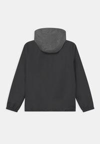 Giacca nera impermeabile con cappuccio grigio, dotata di polsini elasticizzati e una vestibilità rilassata. Texture liscia con un design semplice.