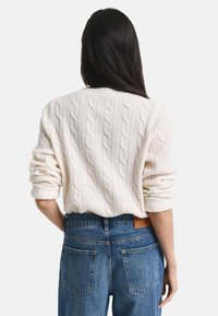 Maglione crema a trecce con scollo rotondo, taglio leggermente oversize, abbinato a jeans in denim blu a vita alta. Design semplice, tessuto testurizzato.