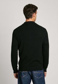 Schwarzer Strickpullover mit rundem Kragen und langen Ärmeln. Gerippte Bündchen und Saum. Kombiniert mit dunkelblauen Jeans.