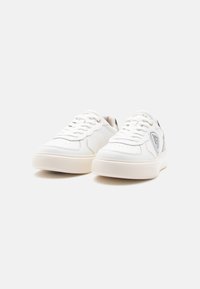 Sneakers bianchi a bassa altezza realizzati in pelle liscia, con suola testurizzata, dettagli perforati e un logo a contrasto sul lato.