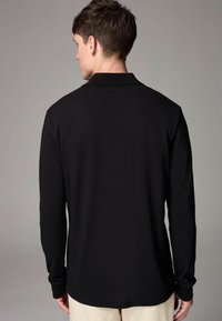 Svart långärmad polo-t-shirt med klassisk krage och mjuk textur, med rak fåll och åtsittande ärmar.