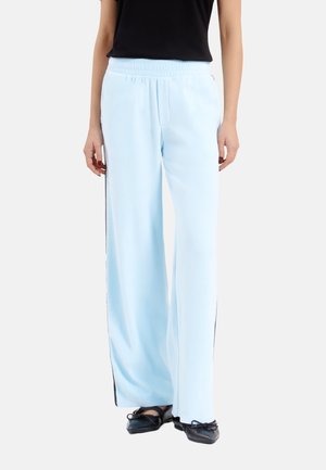 Lichtblauwe wijde broek met een elastische tailleband en zwarte zijstrepen, gemaakt van een soepele stof, gecombineerd met zwarte schoenen.