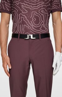 Bordowy polo z konturowym wzorem, w zestawieniu z ciemno bordowymi spodniami. Czarny pasek z metalową klamrą w kolorze srebra oraz na dłoni biała rękawica golfowa.