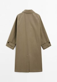 Lang khakifarvet trenchcoat med foldede manchetter sikret med knapper, rygventilation i midten og en klassisk krave på en hvid baggrund.