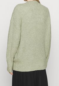 Měkký, světle zelený pletený svetr s žebrovanou texturou, uvolněným střihem a spadlými rameny, s kulatým výstřihem a dlouhými rukávy.