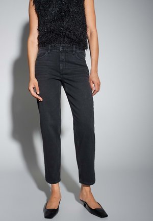 Schwarze High-Waist-Jeans mit geradem Bein, ausgestattet mit dezenten Stickdetails und einem sauberen Finish. Kombiniert mit einem strukturierten schwarzen Oberteil.