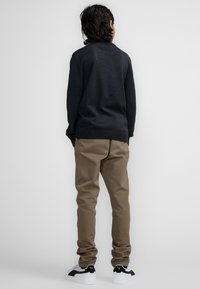 Maglione scuro a maglia, pantaloni khaki e sneakers bianche con accenti neri. Il maglione ha un orlo a coste; i pantaloni si adattano bene e si stringono alla caviglia.