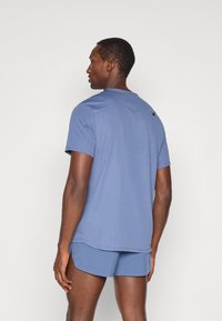 Maglietta sportiva blu a maniche corte, con texture perforata e piccolo logo nero sul retro, abbinata a pantaloni corti coordinati.