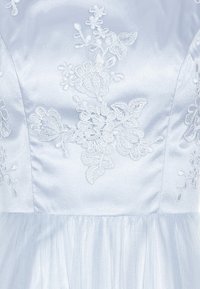 Corsage de robe en satin blanc avec broderie florale en dentelle et une partie de jupe en tulle transparent visible en bas.