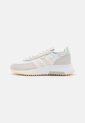 Baskets basses de sport en blanc et beige avec un accent vert clair au talon, des superpositions en daim et une semelle rainurée distinctive pour l'adhérence.