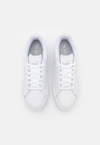 Baskets blanches sportives avec une tige synthétique lisse, un embout arrondi, une fermeture à lacets, un col rembourré et une semelle extérieure en caoutchouc texturée.