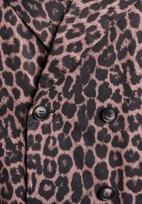 Blazer en imprimé léopard en tissu doux, avec un design croisé, des boutons noirs, et des détails de motifs contrastants en noir et rose.
