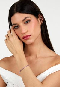 Bracciale di gemme viola con accenti in argento, caratterizzato da una forma delicata e curva. Modella che lo indossa, con un top bianco semplice a spalla scoperta.