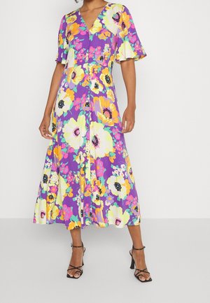 Robe maxi à motifs floraux avec un fond violet et des fleurs jaunes, roses et vertes. Décolleté en V, manches courtes en volants et silhouette fluide.