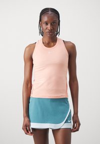 Top sport Nike într-o nuanță de piersici moi, cu decolteu rotund și croială slim, combinat cu o fustă teal cu accente albe și un design înfășurat.