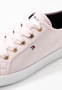 Růžové plátěné tenisky se světle růžovými pruhovanými tkaničkami, zlatými očky a bílou gumovou podrážkou. Na boku mají malou vyšívanou nášivku.