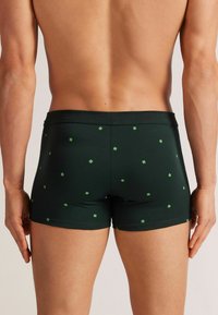 Tmavě zelené boxerky vyrobené z elastického materiálu, s vzorem malých zelených čtverců. Elastický pas pro pohodlné nošení.