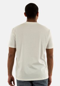 T-shirt en coton blanc avec manches courtes et col rond, vu de derrière. Présente une texture lisse et une coupe décontractée.
