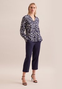 Blusa a pois navy con scollo a V e maniche lunghe, abbinata a pantaloni navy aderenti e tacchi neri con cinturino alla caviglia. Tessuto liscio e vestibilità su misura.