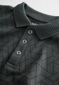 Mörkgrå polo skjorta med geometriskt mönster, ribbad krage och tre metalliska knappar. Mjuk tygtextur.