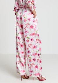 Florale, weit geschnittene Hose aus leichtem Stoff, mit rosa Aquarellblumen auf weißem Hintergrund, seitlichen Taschen und lockerem Schnitt.