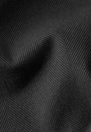 Gros plan sur un tissu gris foncé avec une texture tissée en chevrons et des plis subtils créant de la profondeur et des ombres.