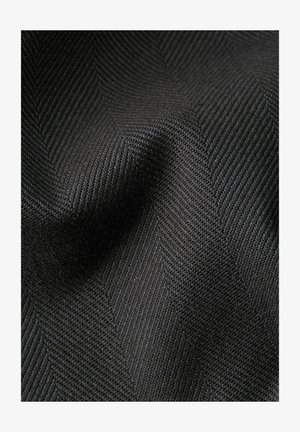 Primo piano di tessuto grigio scuro con trama a zigzag intrecciata e pieghe sottili che creano profondità e ombre.