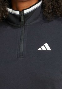 Pullover nero con zip, realizzato in tessuto morbido. Presenta un logo Adidas bianco e un colletto a strati con accenti grigi e bianchi.