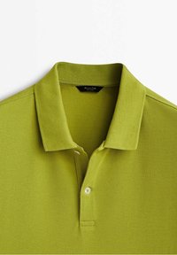 Polo vert clair à manches courtes avec col et deux boutons, posé à plat sur un fond blanc.