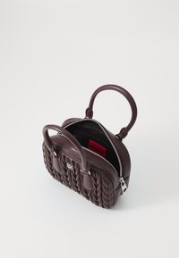 Borsa a mano in pelle bordeaux con texture trapuntata, due manici corti, chiusura a zip e un interno nero a contrasto con un'etichetta rossa.