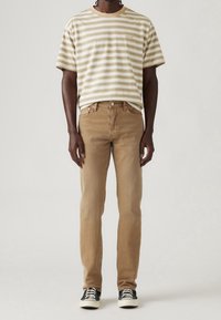 T-shirt rayé beige et blanc avec un col rond ; jean couleur beige ; baskets noires et blanches. Coupe décontractée avec coutures visibles et poches.