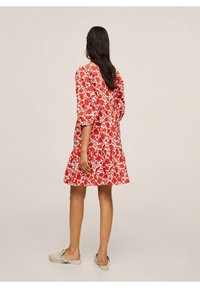 Robe imprimée florale rouge avec des manches 3/4, une jupe évasée et un col rond. Le tissu est léger avec une texture douce. Chaussures décontractées.
