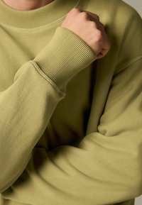 Világos olíva zöld pulóver ribbelt mandzsettákkal és nyakkivágással. Puha, textúrált anyag, lazán illeszkedő fazonnal és varrás nélküli dizájnnal.