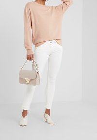 Pull rose clair, jeans skinny blancs, mules à talons crème et sac à main beige avec bandoulière chaîne, mettant en valeur un design élégant et une texture lisse.