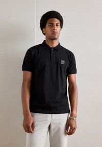 Zwarte polo met korte mouwen van katoen, met een geribbelde kraag, een drieknopenlijst en een klein logo-embleem op de borst.