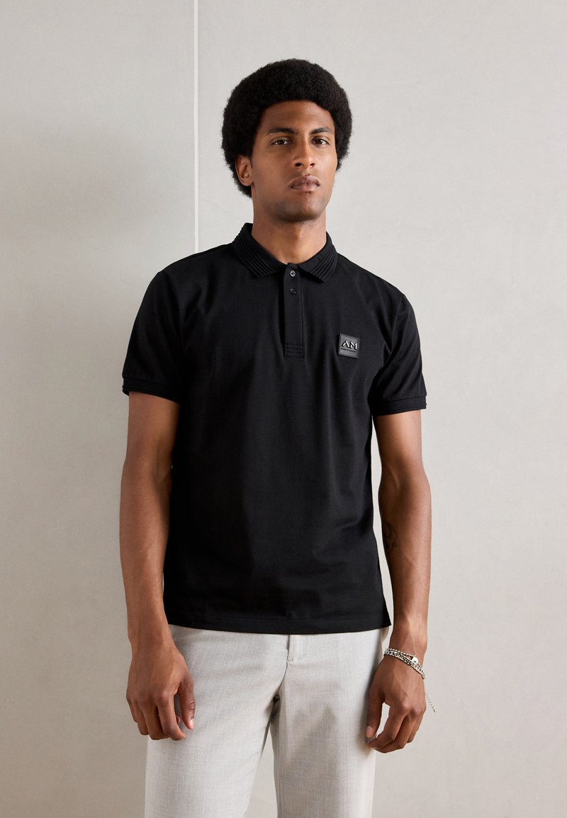 Zwarte polo met korte mouwen van katoen, met een geribbelde kraag, een drieknopenlijst en een klein logo-embleem op de borst.