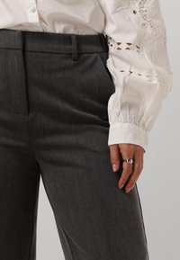 Grijze op maat gemaakte broek met een soepele textuur, voorzien van zijzakken en een vlakke voorkant. Een witte blouse met lange mouwen en geborduurde details gaat erbij.