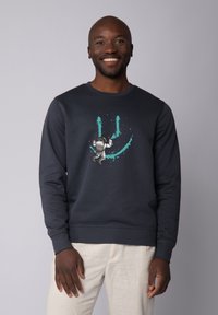 Sweatshirt bleu foncé en coton, arborant un graphique d'astronaute ludique en blanc et teal. Encolure ronde classique et manches longues.