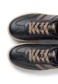 Paire de baskets en cuir noir avec lacets beiges et semelles beiges, avec des bandes latérales et une fermeture éclair sur le côté intérieur de chaque chaussure.