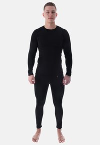 Schwarzes Langarmshirt und Leggings aus dehnbarem Stoff, mit einer figurbetonten Passform und glatter Textur, das Modell zeigt barfuß.