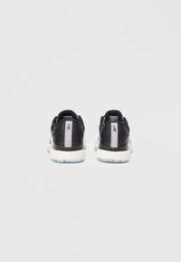 Paita mustia ja valkoisia urheilukenkiä katsottuna takaa, jossa on valkoinen pystyraita ja tekstuurilliset pohjat yksinkertaisella taustalla.