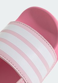 Rosa halksandal med vita ränder, tillverkad av texturerat syntetmaterial. Har en formad innersula och stickade detaljer längs kanterna.