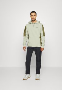 Light green fleece hoodie with an adjustable hood, zippered neck, and olive green shoulder panels. Paired with black pants and white shoes.