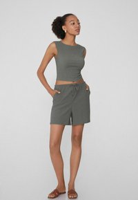 Top corto a coste grigio e pantaloni shorts abbinati con vita elastica e lacci; il modello sta in piedi con le mani nelle tasche e indossa sandali aperti marroni.