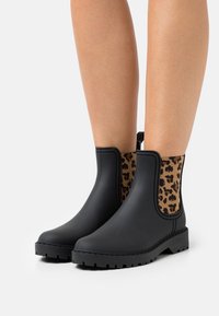 Black waterproof ankle boots with leopard print elastic sides, rugged sole, and pull tab. Smooth matte finish with contrasting textured accents.