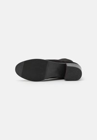 Bota de tornozelo em camurça preta com uma sola de borracha texturizada, apresentando um salto bloco baixo e uma forma suavemente afunilada.