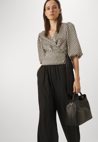 Svart-hvitt mønstrete innpakningsbluse med pufferm, knyttet i midjen, sammen med løse svarte bukser og en svart lærveske.