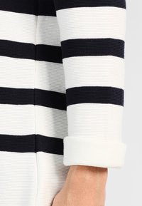 Sweter w paski w kolorze granatowym i białym z poziomymi paskami, wykonany z teksturowanego dzianiny, z podwiniętymi mankietami, podkreślający kontrastujące kolory i wzory.