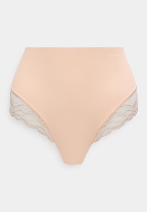 Béžové dámské spodní prádlo s vysokým pasem, zdobené krajkou na okrajích nohaviček a malým logem Calvin Klein na pravé straně pasu.