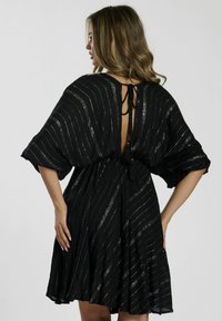 Vestido negro con rayas horizontales plateadas, diseño de espalda en V, mangas sueltas, cinturón en la cintura con borlas y falda fluida. Tejido ligero.